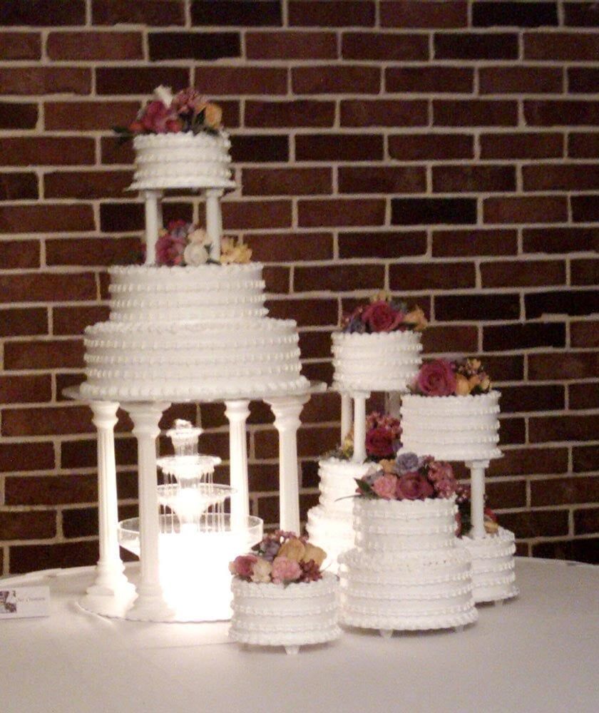 Wedding cake display with tiered white cakes, floral accents, and fountain structure.