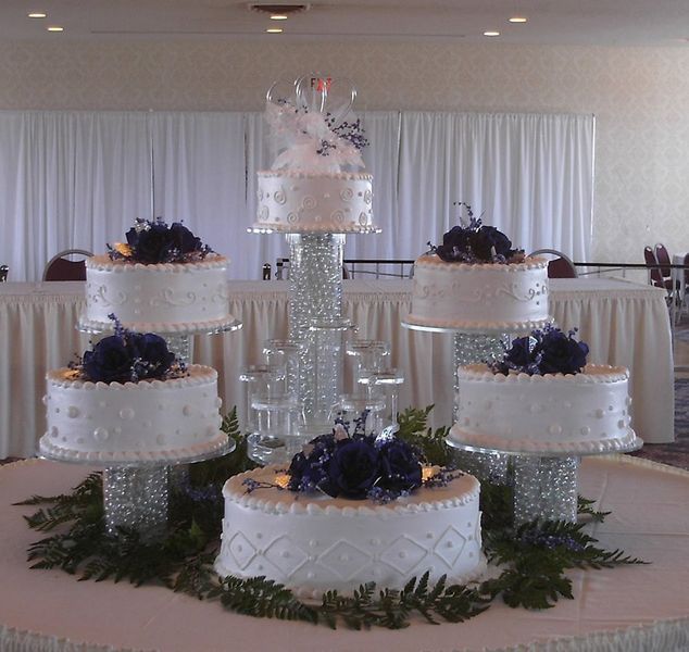 Multi-tiered white wedding cake with blue floral accents, on a table.