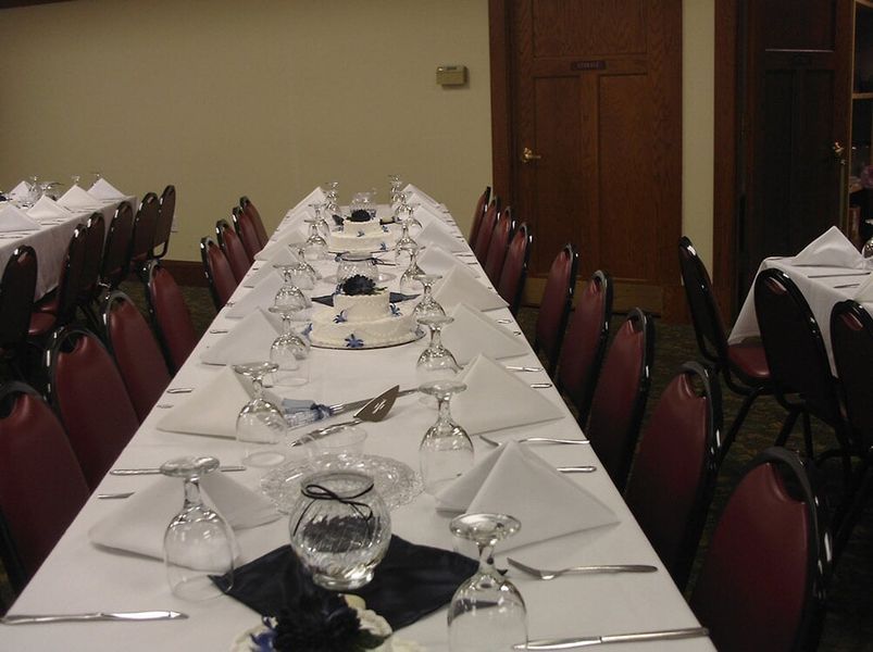 Long dining tables set for a formal event with white linens, red chairs, and tableware.