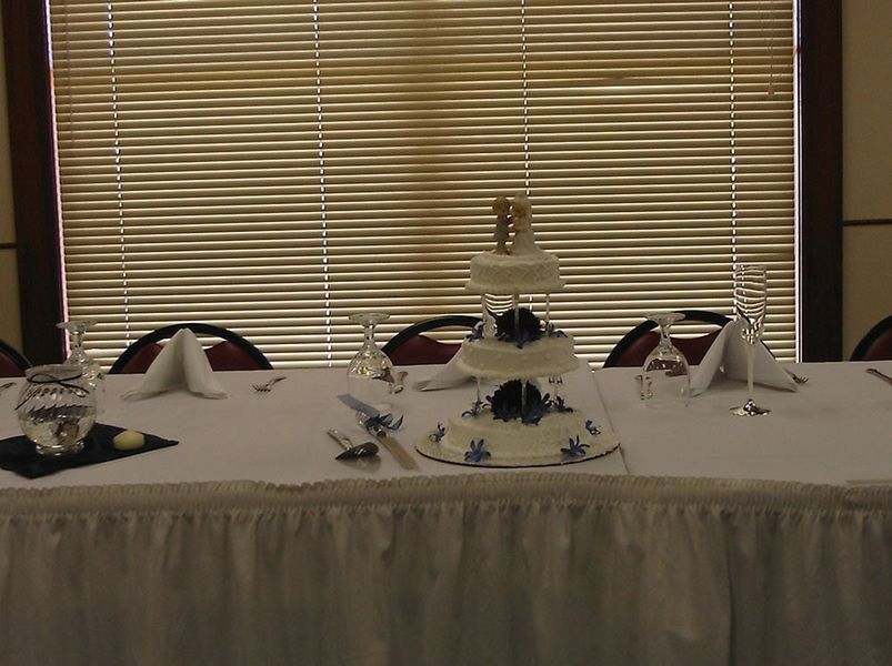 Wedding cake on a table set for a celebration, with a window and chairs in the background.