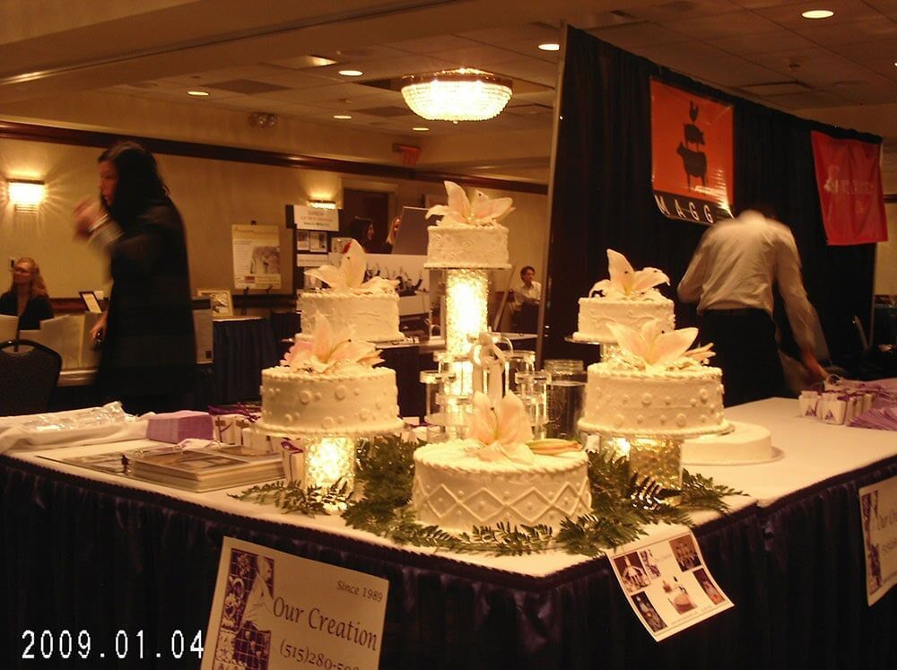 Wedding cakes on display at a vendor booth. White frosted cakes with floral decorations, in a convention hall.