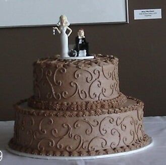 Two-tiered chocolate cake with swirled frosting and a bride and groom cake topper.
