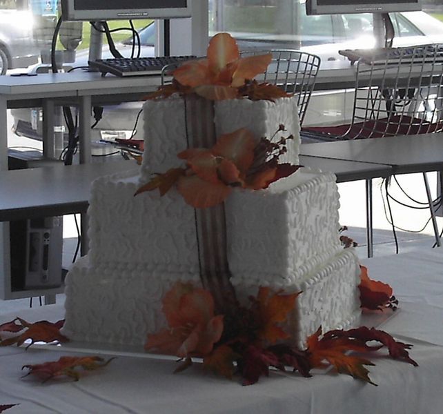 Three-tiered square wedding cake decorated with orange flowers and fall leaves, on a table.