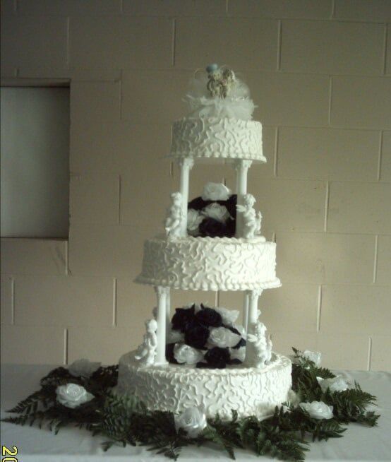 Four-tiered white wedding cake with pillars, decorated with flowers and greenery, on a table.