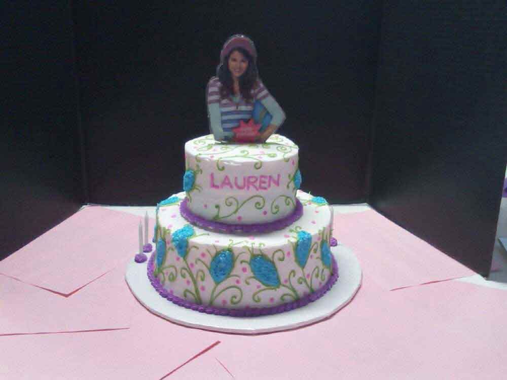 Two-tiered cake with a photo of a person on top, purple, blue, and green decorations, the name 