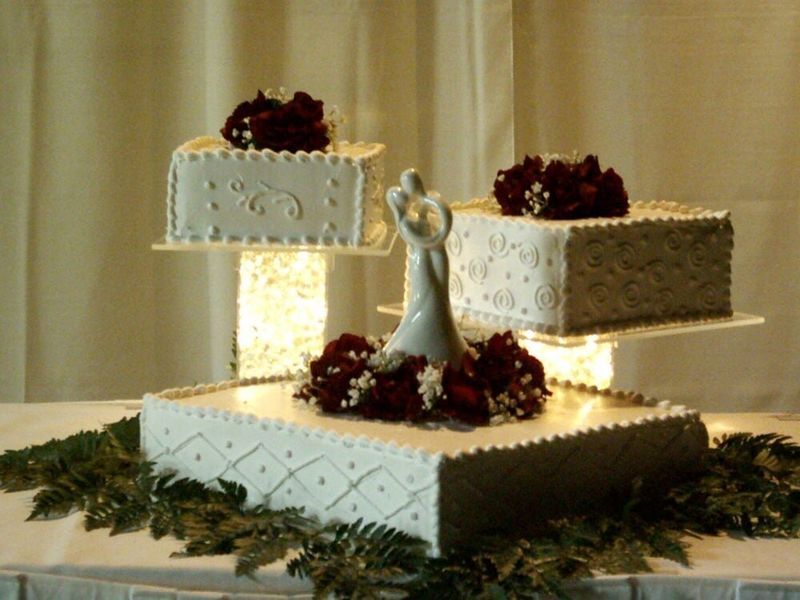 Three-tiered square wedding cake with floral accents and a bride and groom figurine.