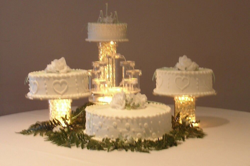 Wedding cake display: White tiered cakes with floral decorations, lit from below, on a table.