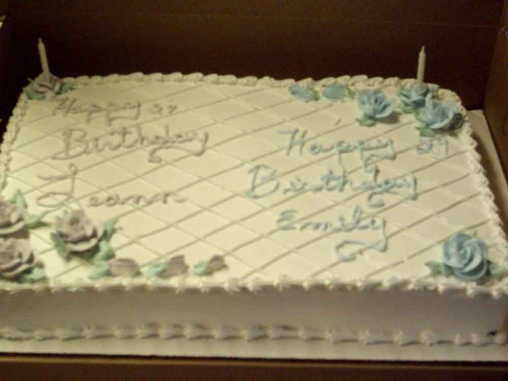 White rectangular birthday cake with piped writing and blue and purple frosting roses.