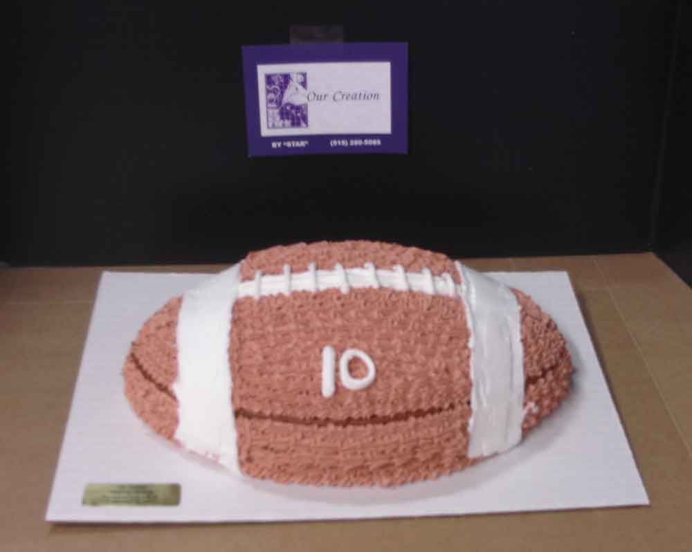 Football-shaped cake with brown frosting, white stripes, and the number 10, on a white board.