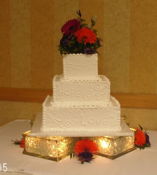 Three-tiered white wedding cake with floral topper, on a lighted crystal base; 