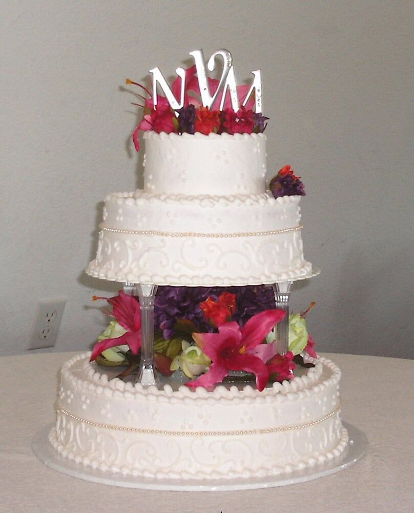 Three-tiered white wedding cake decorated with flowers and a 