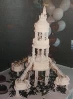 Wedding cake, white, tiered, tower-like structure with small side cakes, balloons in the background.