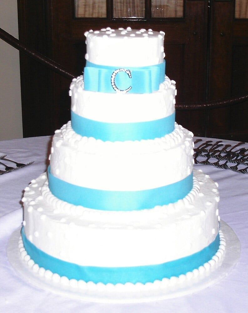 Four-tiered white cake with turquoise ribbon, pearl accents, and a jewel 