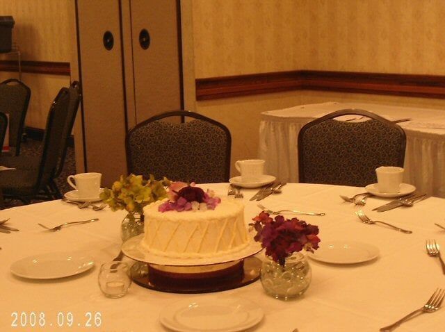 A round table set for a formal event with a cake, flowers, and place settings.