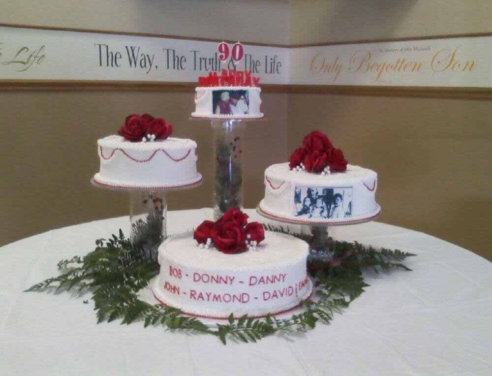 Four-tiered cake display for a 90th birthday celebration with red roses and names on the bottom tier.