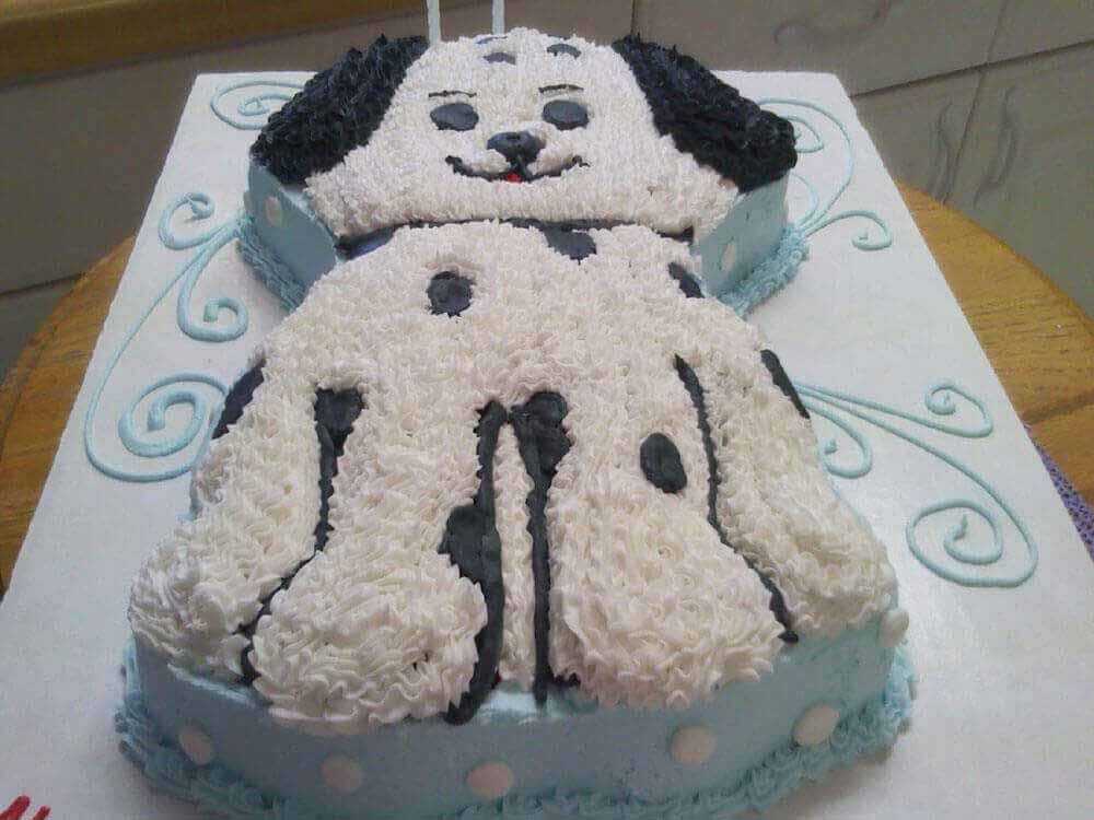 Dog-shaped cake, white frosting with black spots. Blue base and accents. Birthday cake.