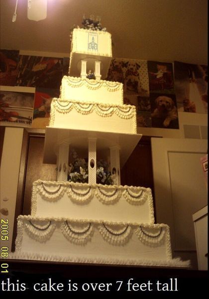 Tall, five-tiered white cake with decorative frosting and a small top tier. In a room, likely a home.