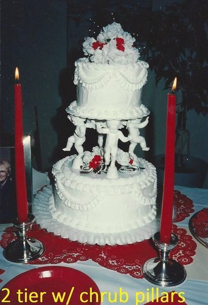 Wedding cake with three tiers and cherub pillars, red candles.