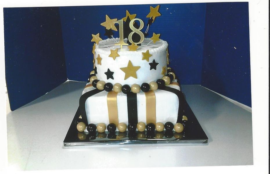 Two-tiered birthday cake, white frosting with gold and black accents. Gold stars and 