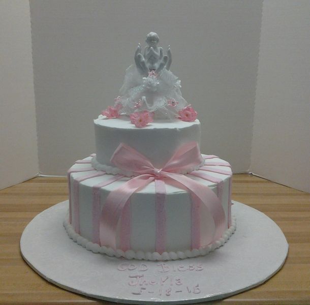 Two-tiered white cake with pink ribbon and flowers, topped with a figure on a round base.