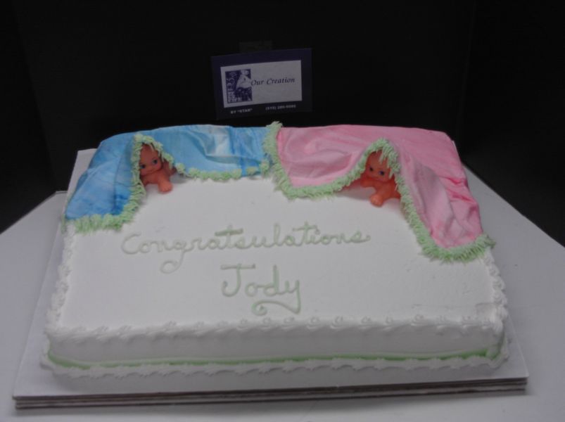 Cake decorated for twins, with blue and pink covers, frosting babies, and 