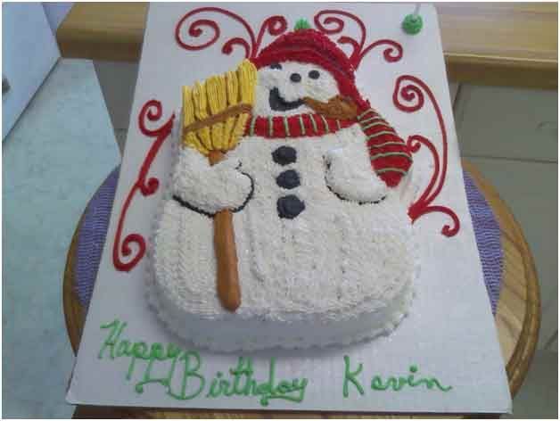 Snowman-shaped birthday cake with a red hat and scarf, holding a broom, with 