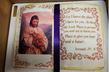 Cake decorated as an open book, featuring an image of Jesus holding a lamb and a Bible verse.