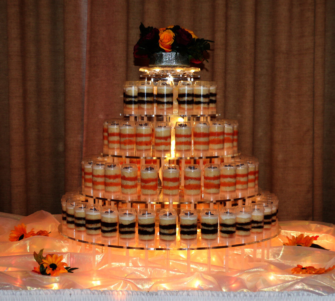 Tiered shot glass display with alternating orange, black, and white layers, topped with flowers.