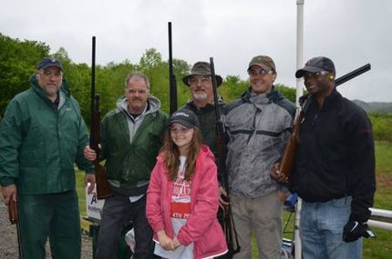 Group of people, some with shotguns, at an outdoor shooting range; overcast day.