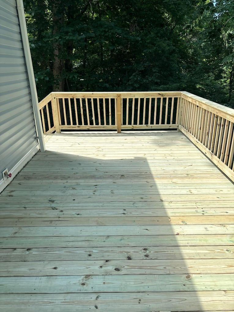A large wooden deck with a wooden railing and trees
