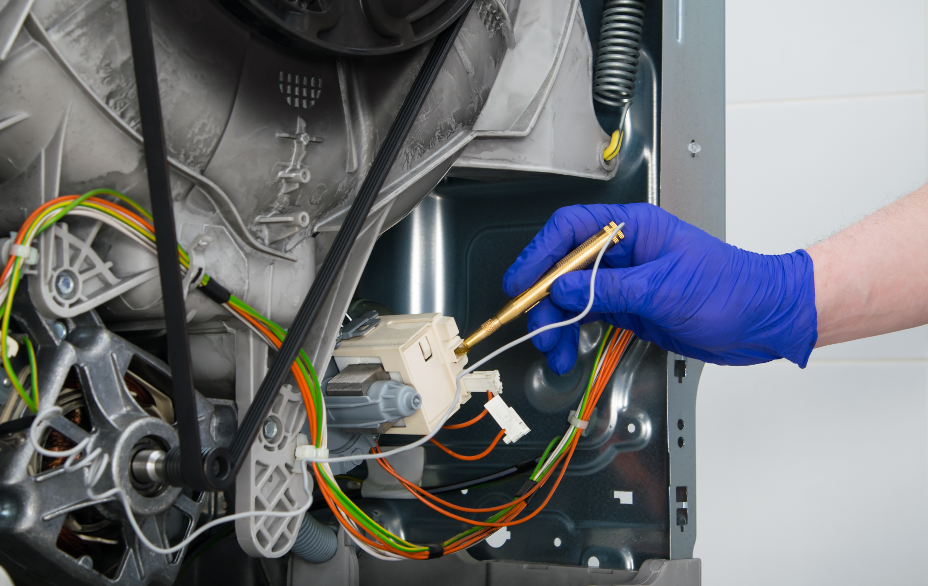 Gloved hand holding a test probe inside an open electronic device with tangled colored wires