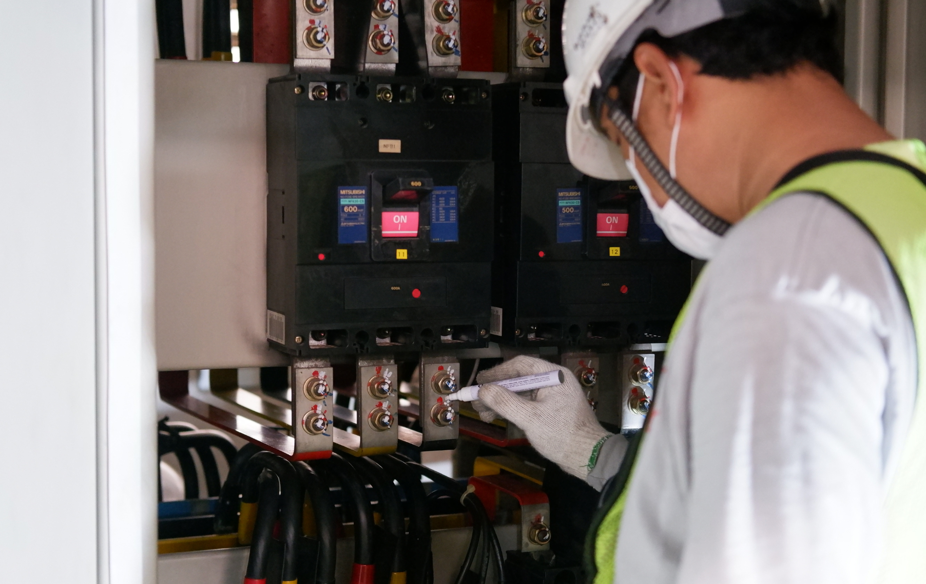 Technician inspecting electrical control panel with tools in a utility cabinet