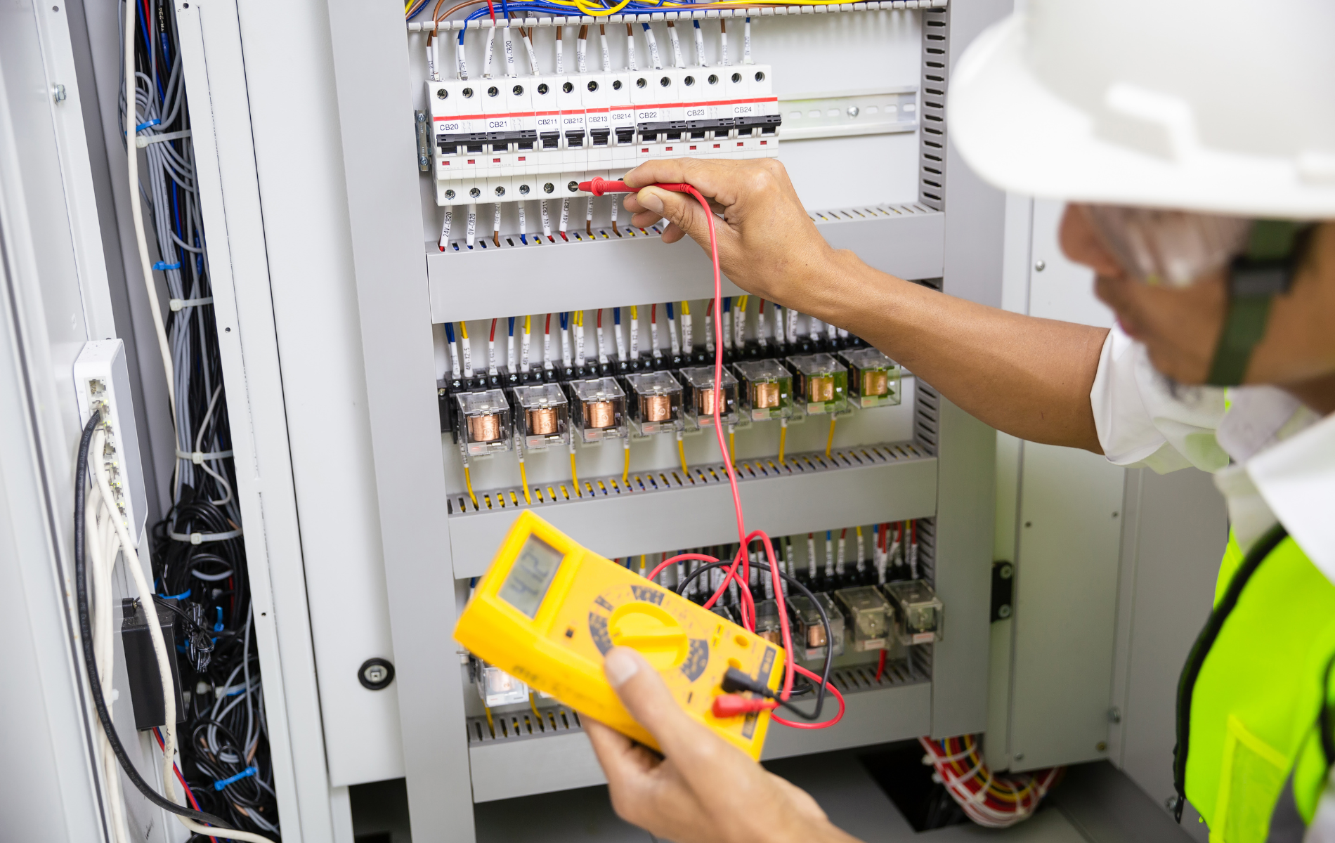 Technician testing a circuit breaker panel with a yellow multimeter in an electrical cabinet