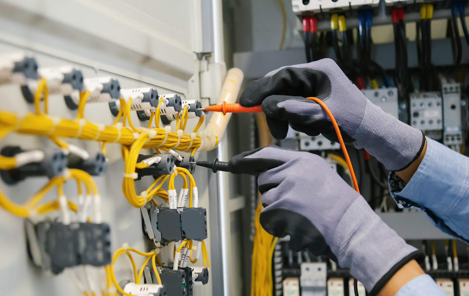 Technician in gray gloves wiring an electrical control panel with yellow cables and tools