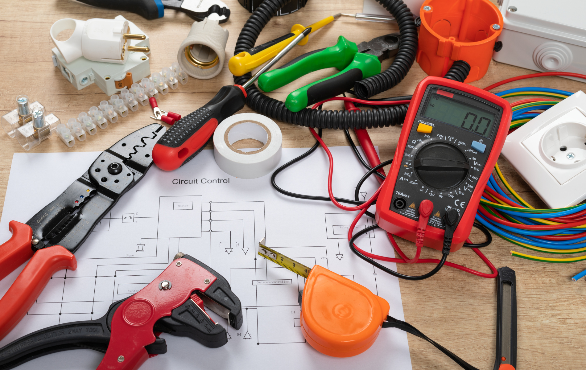 Electrical tools and supplies scattered on a workbench with a red multimeter and wire cutters