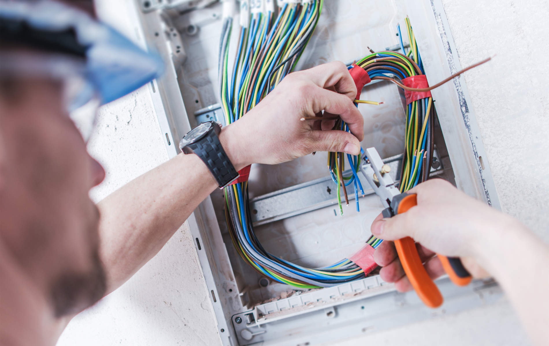Technician wiring an electrical panel with colorful cables and orange pliers