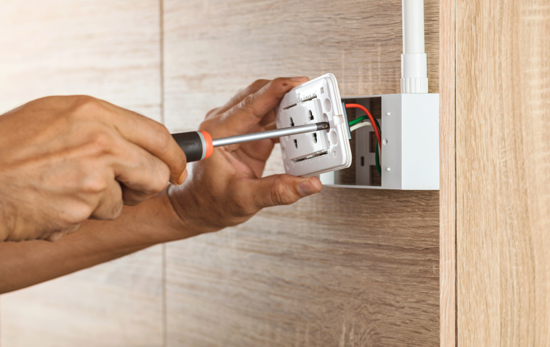 Hands using a screwdriver to install an electrical outlet on a wall