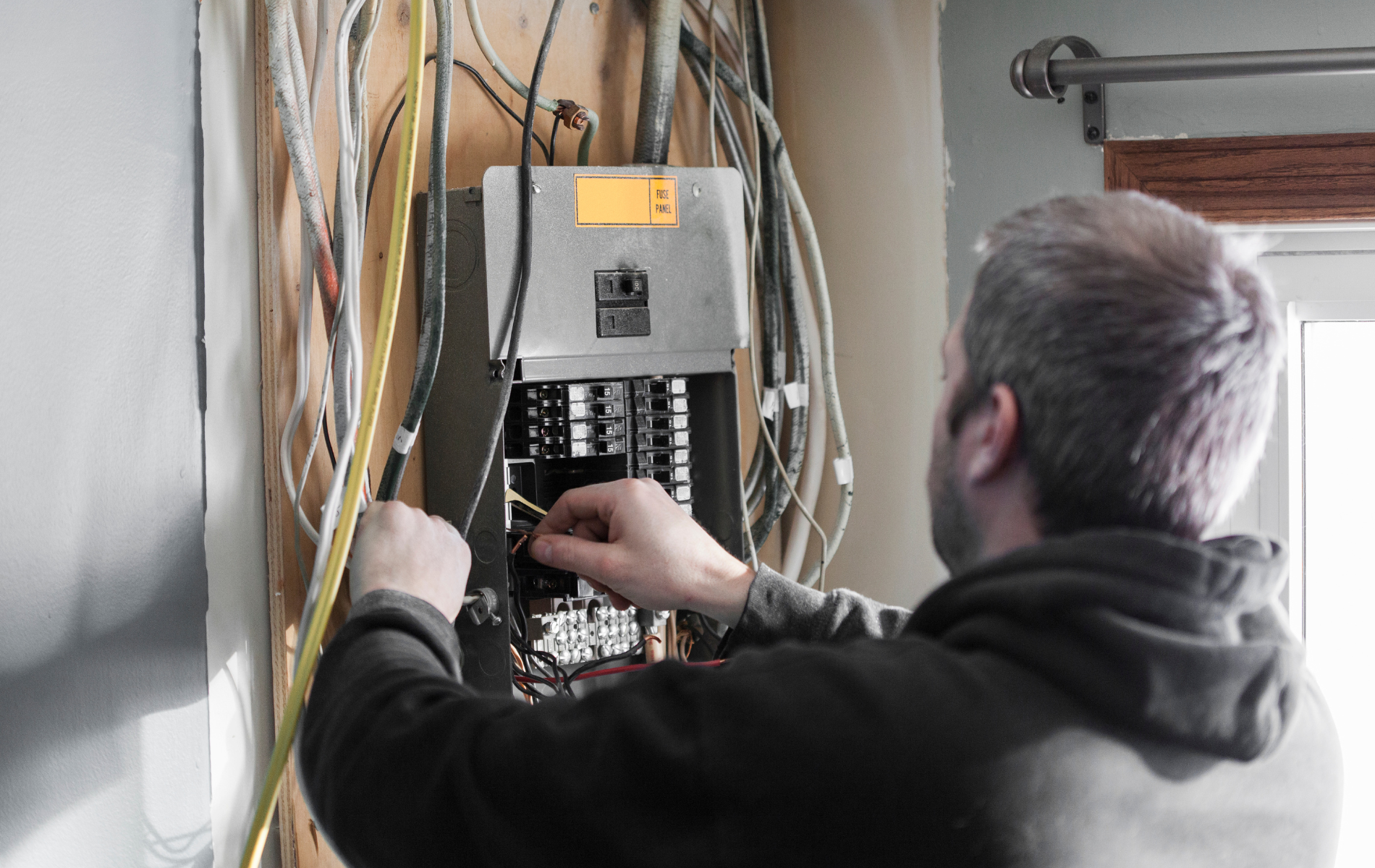 Technician wiring an electrical panel in a utility room, with cables and circuit breakers visible.