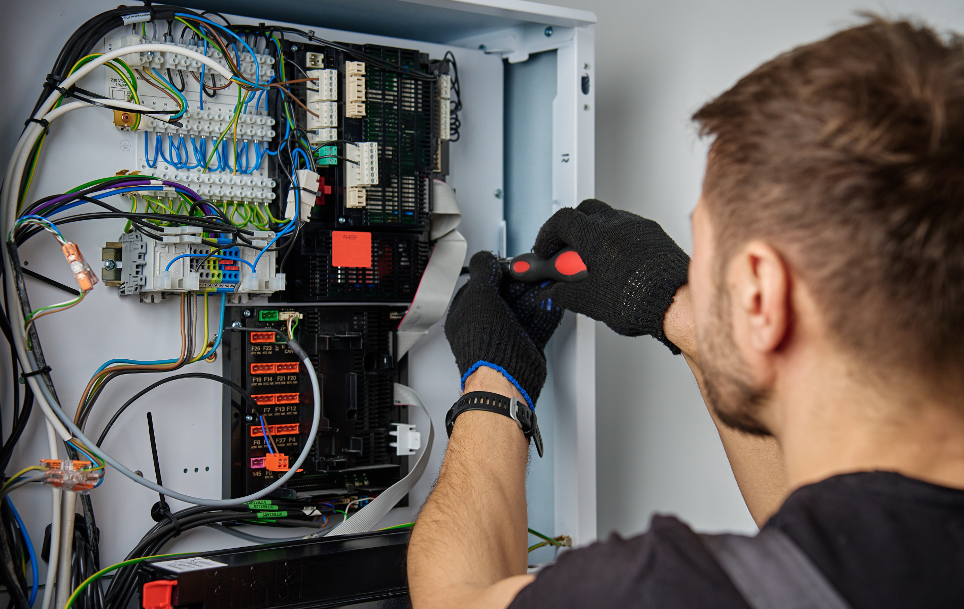 Technician working inside an open electrical control panel, adjusting wiring with a screwdriver.