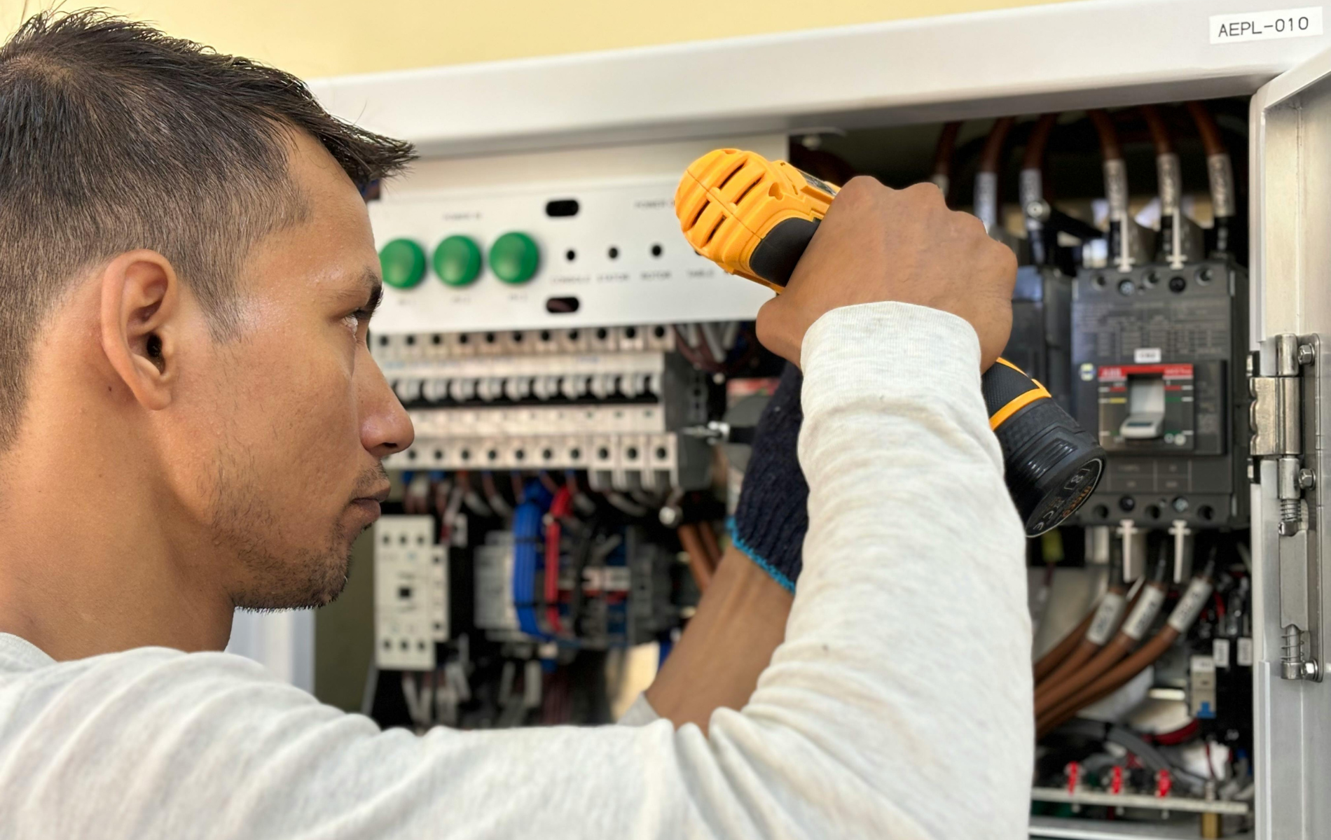 Technician using a drill to work inside an open electrical panel.