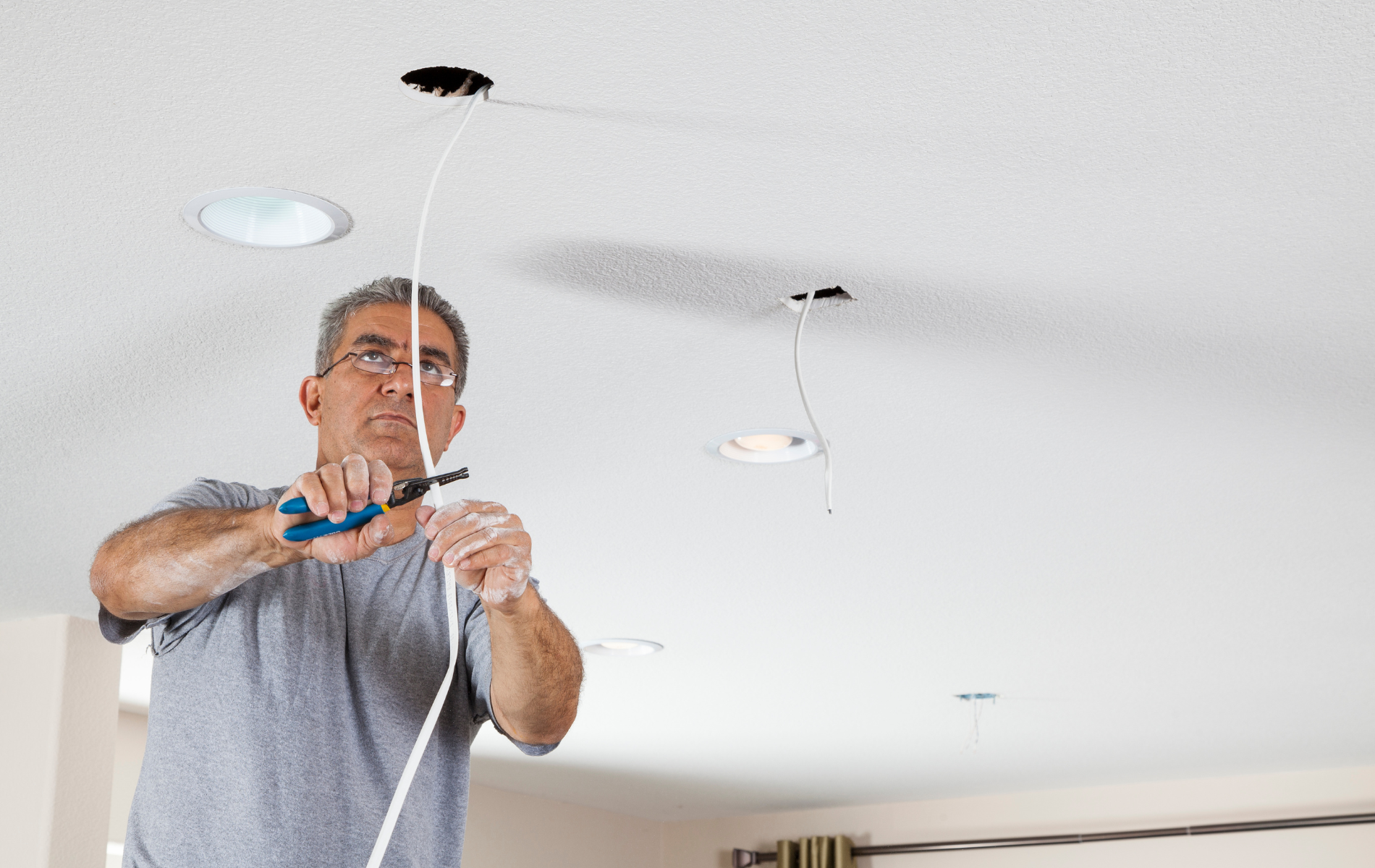 Man installing a ceiling light fixture with tools in a white room