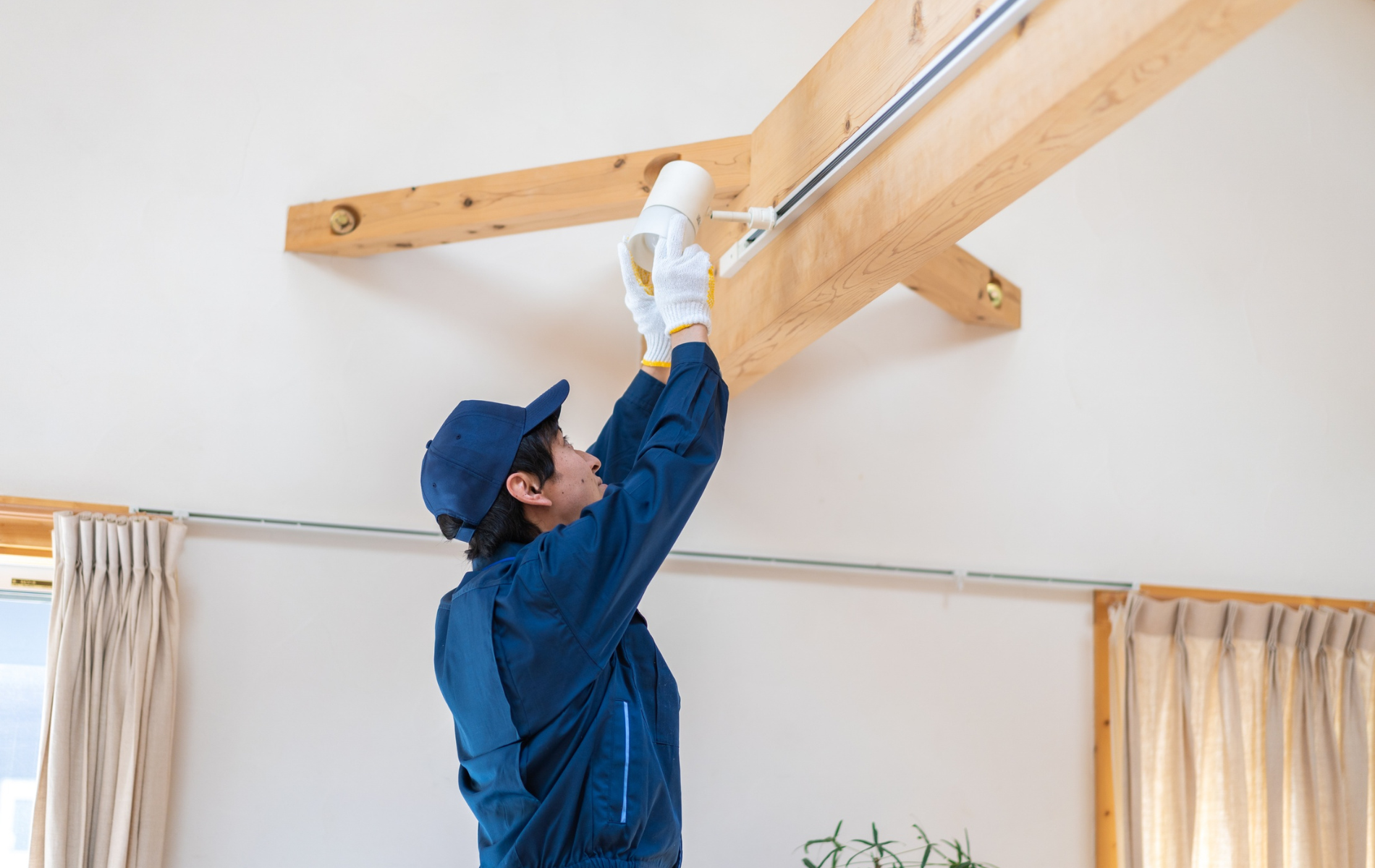 Worker in blue uniform adjusting a ceiling-mounted wooden beam indoors