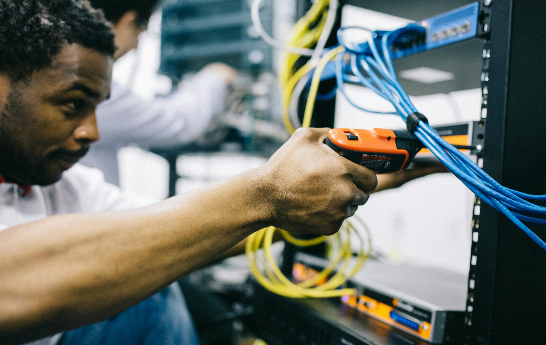 Technician using a handheld scanner to inspect server rack cables in a data center