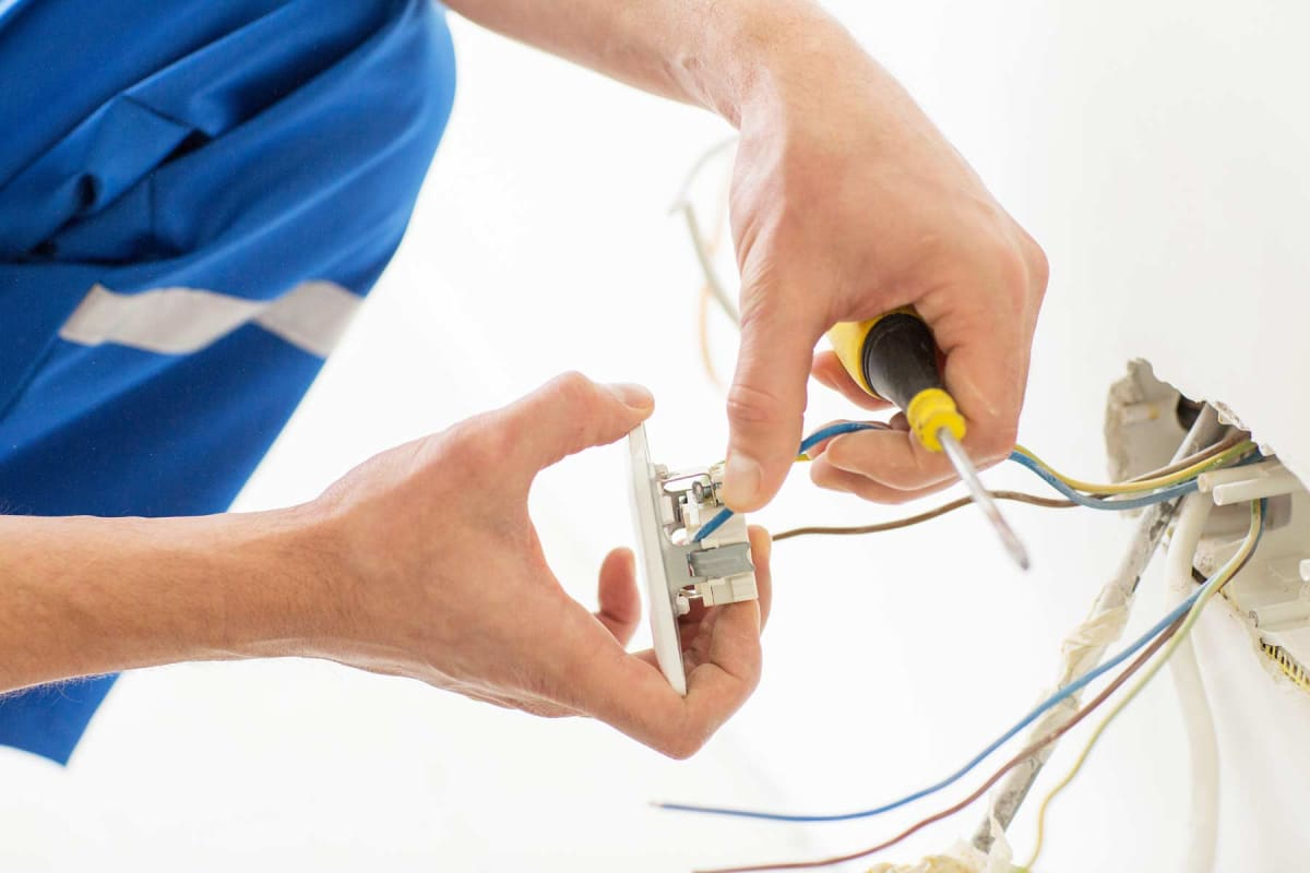 Electrician wiring a wall outlet with blue and yellow tools and exposed cables