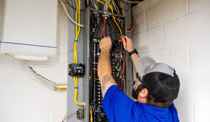 Technician wiring an open electrical panel with exposed cables in a utility room