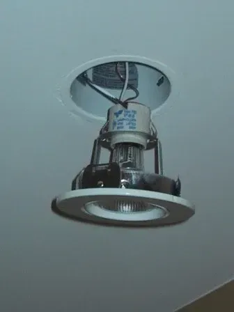 Ceiling-mounted recessed light fixture hanging loose with exposed wiring and chrome trim