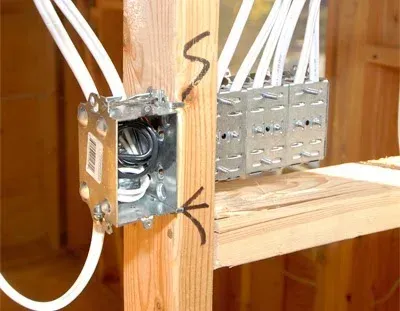 Electrical junction boxes and white cables mounted on wooden studs in a wall framing area