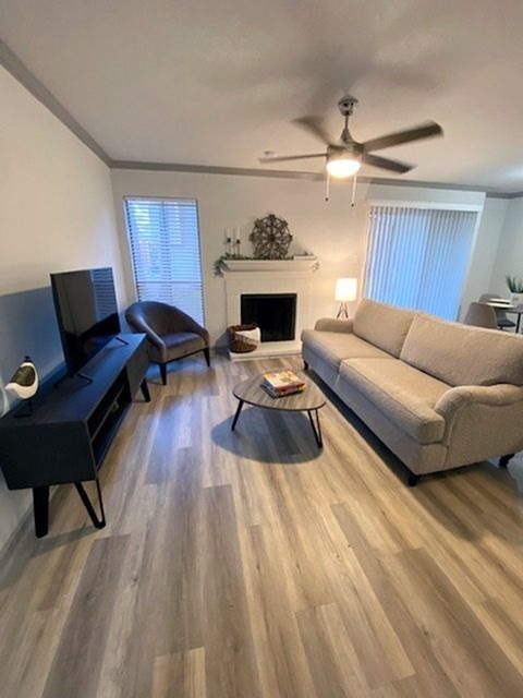 Living room in an apartment with a beige sofa, chair, fireplace, TV, and ceiling fan.