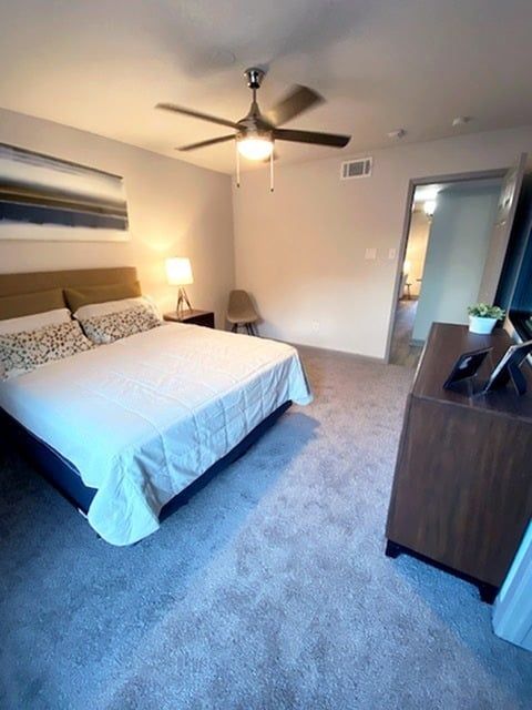 Bedroom in an apartment with a large bed, ceiling fan, dresser, and doorway.