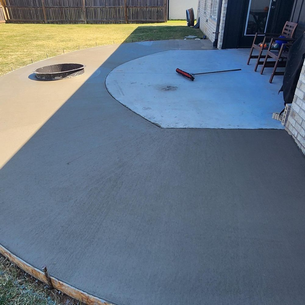A concrete patio with a fire pit and chairs in the backyard.